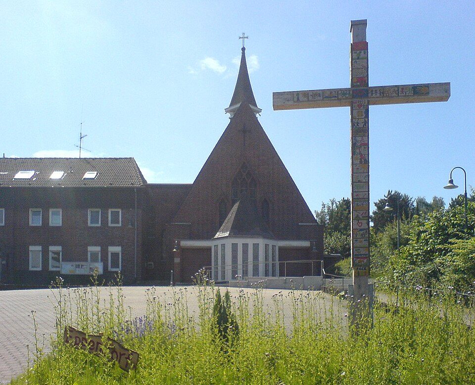 Backsteinkirche mit spitzem Turm und hohem Kreuz auf dem Vorplatz in Bochum-Wattenscheid-Eppendorf