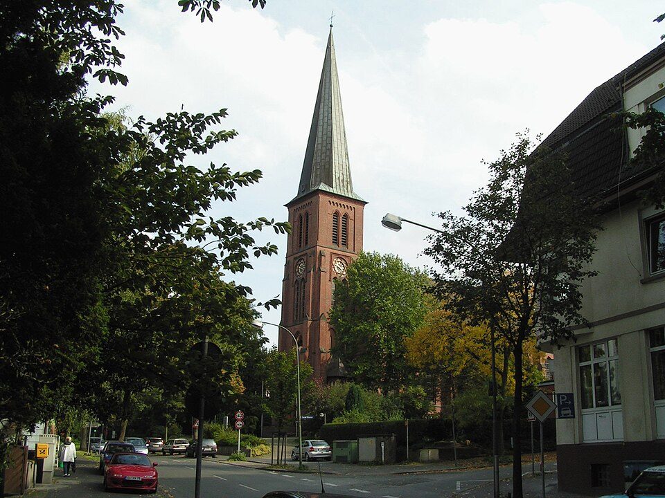 Wohnstraße mit Bäumen, älteren Wohnhäusern und dem Backsteinturm der Liboriuskirche in Bochum-Grumme