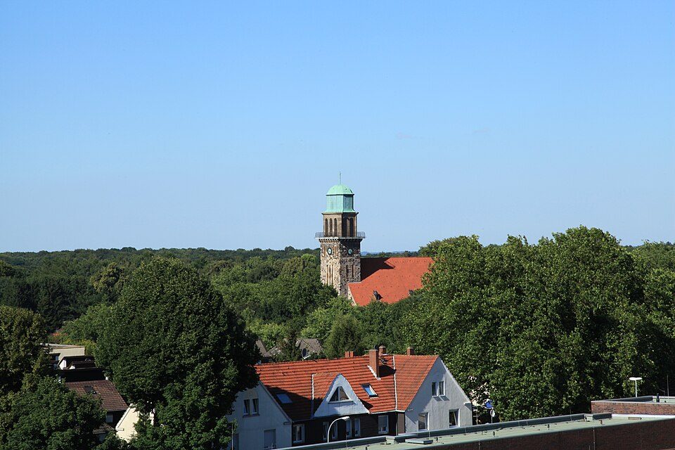 Der Turm der Erlöserkirche über den Dächern von Wohnhäusern und viel Grün in Bochum-Hiltrop