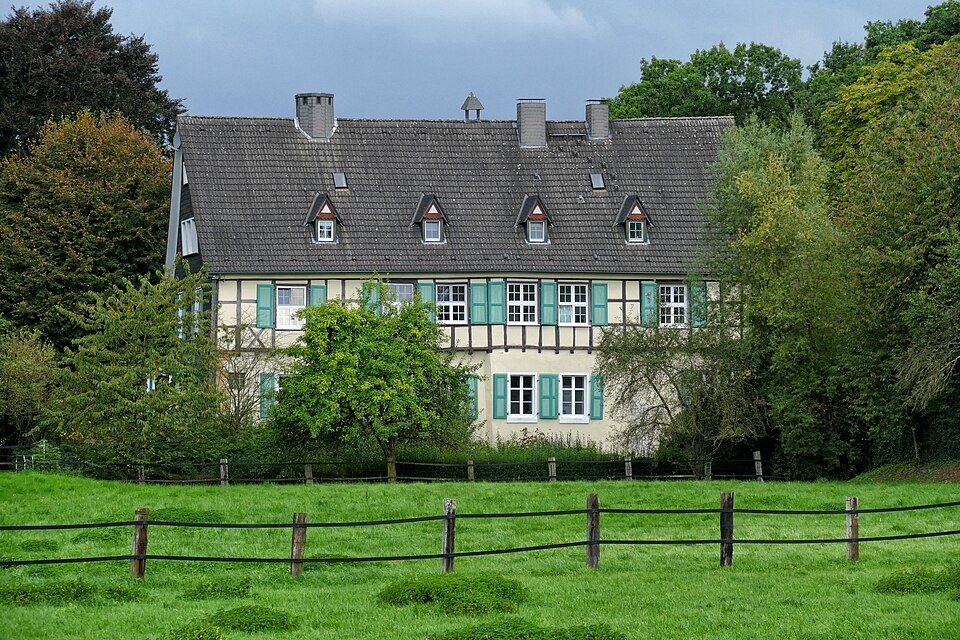 Fachwerk-Herrenhaus Haus Laer mit grünen Fensterläden hinter einem Holzzaun und einer Wiese in Bochum-Laer