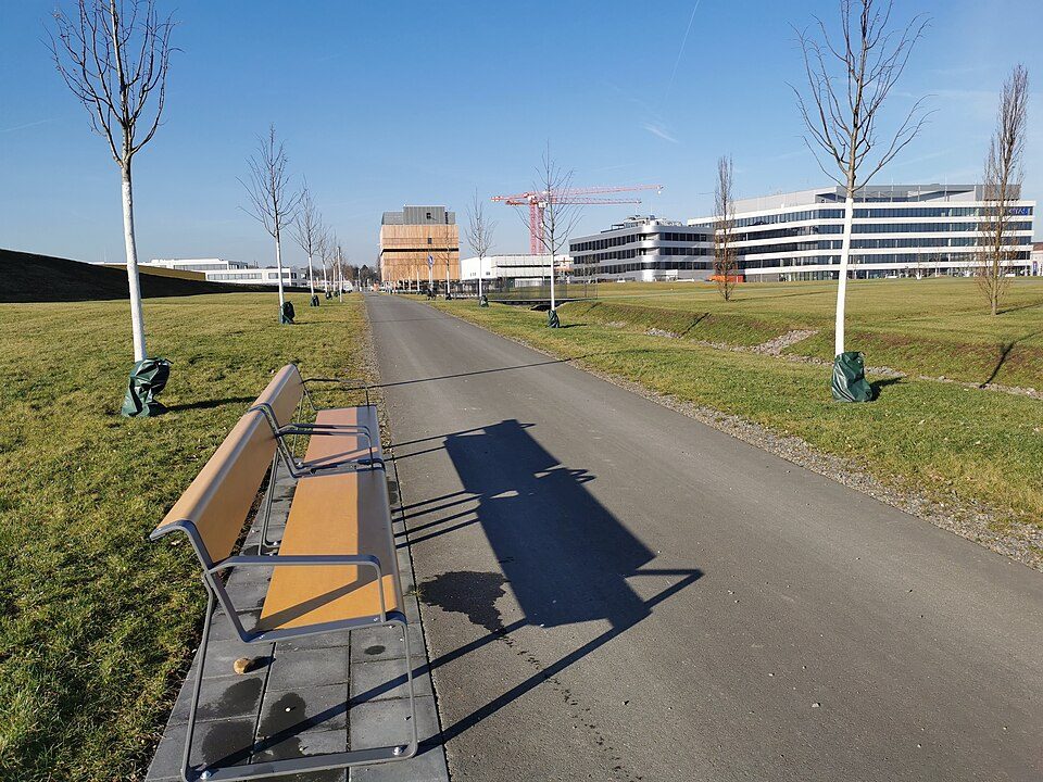Fußweg mit Sitzbank und jungen Bäumen auf dem Gelände MARK 51°7 in Bochum-Laer, im Hintergrund neue Bürogebäude und ein Baukran