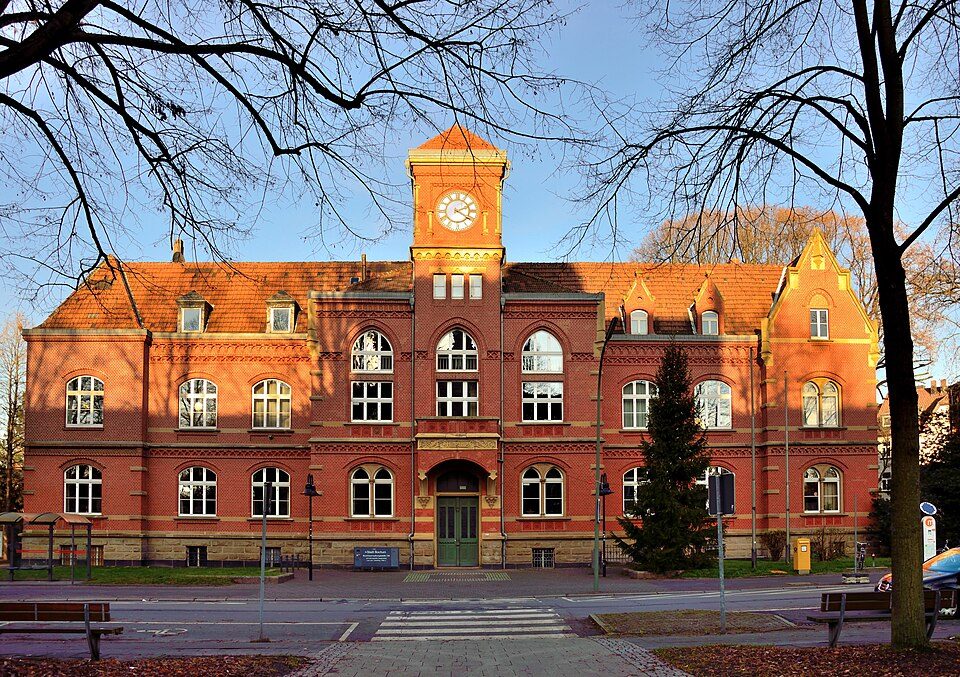 Altes Amtshaus Langendreer aus rotem Backstein mit Uhrturm am Carl-von-Ossietzky-Platz, davor Bäume und Bänke