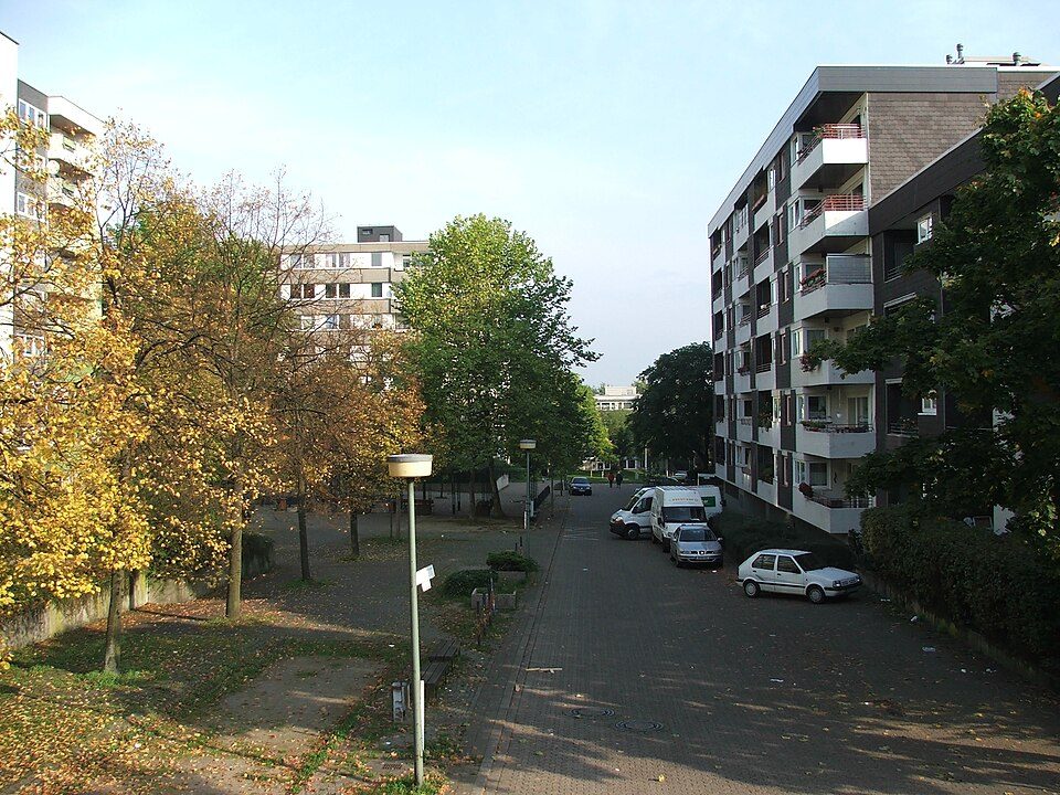 Mehrgeschossige Wohnhäuser mit Balkonen in der Hustadt in Bochum-Querenburg, dazwischen ein gepflasterter Weg, Laternen und Bäume im Herbstlaub