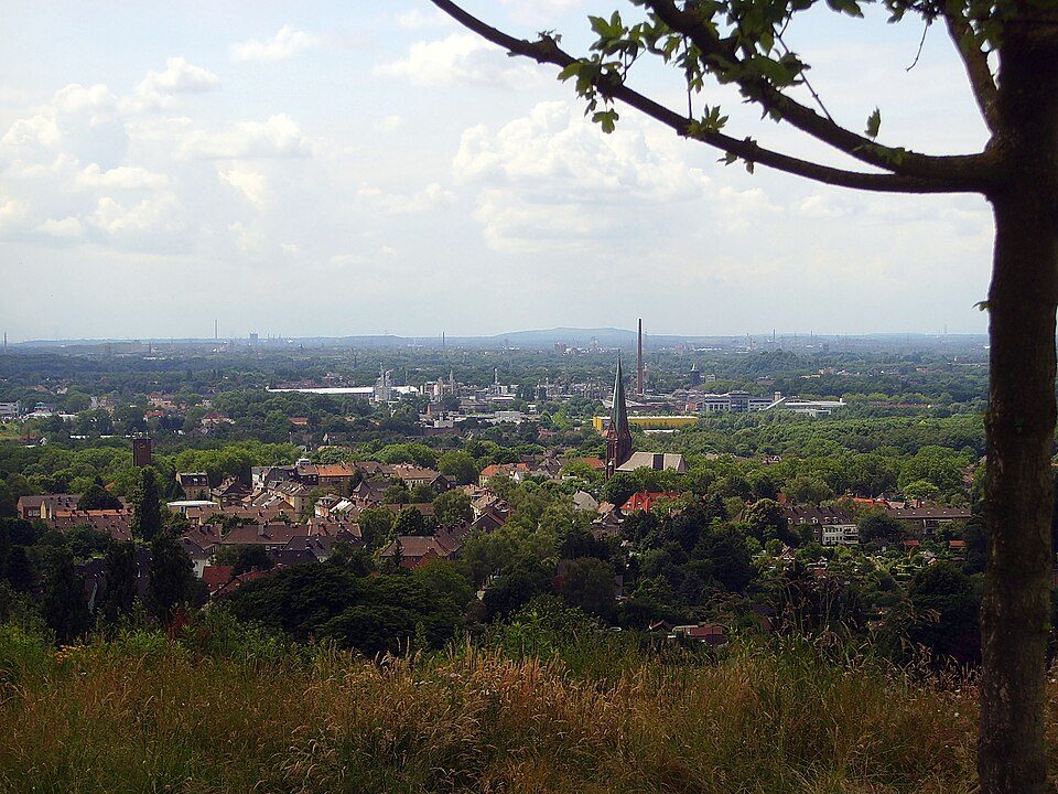 Blick vom Tippelsberg über die Dächer und Gärten von Bochum-Riemke mit Kirchturm, im Hintergrund das Ruhrgebiet
