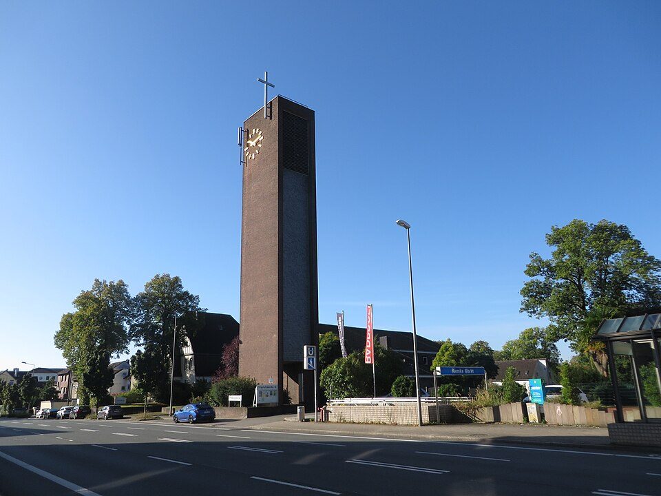 Herner Straße in Bochum-Riemke mit dem hohen Backsteinturm der Trinitatiskirche, Bäumen und parkenden Autos