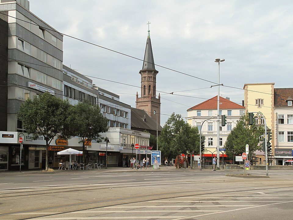 Bahnhofstraße im Zentrum von Wattenscheid mit Straßenbahnschienen, Geschäftshäusern und dem Backsteinturm der Friedenskirche