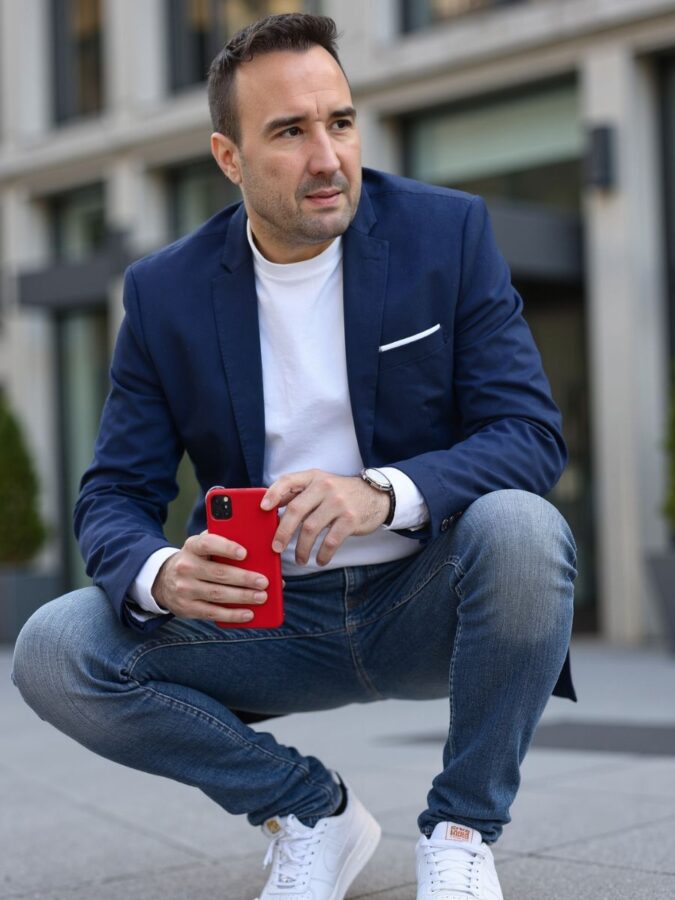 Christian Gottschling in der Hocke vor einem modernen Gebäude, ein Smartphone in der Hand